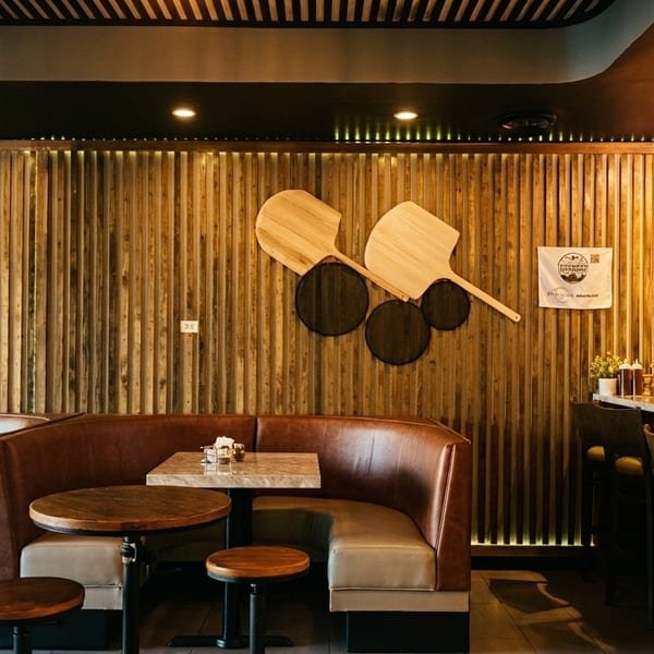 Cozy restaurant interior with brown leather booths, marble tables, a wooden slatted wall, and a full bar.
