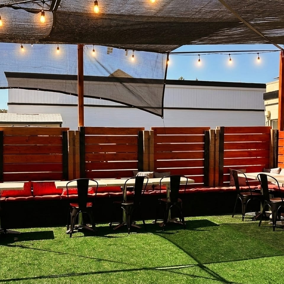 Outdoor patio with artificial turf, string lights, wooden fences, and tables with red cushioned benches.