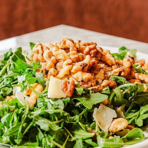 Arugula salad with walnuts and parmesan cheese on a white plate.