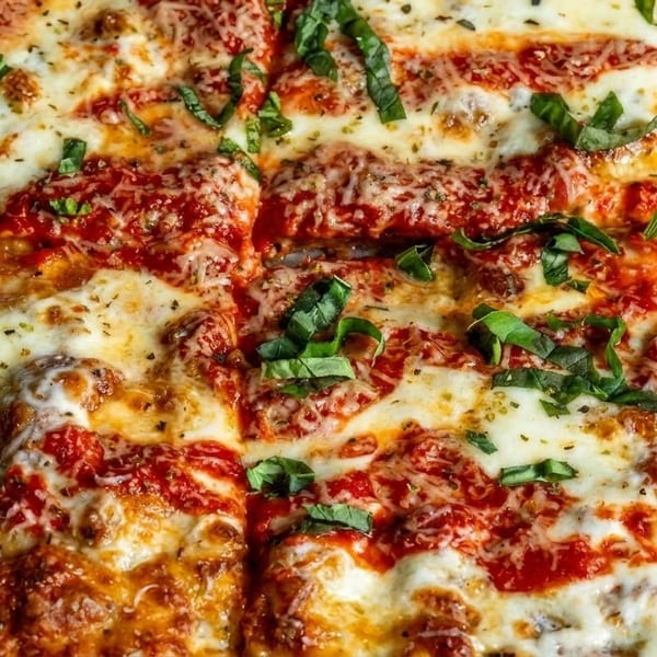 Close-up of a rectangular pizza with melted cheese, red sauce, and fresh basil leaves.